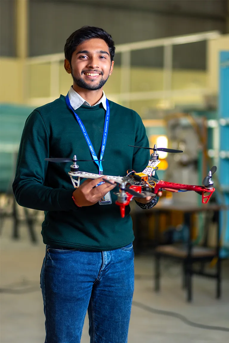 A student smiles holding a drone, representing BTech Aeronautical Engineering Colleges in Bangalore.
